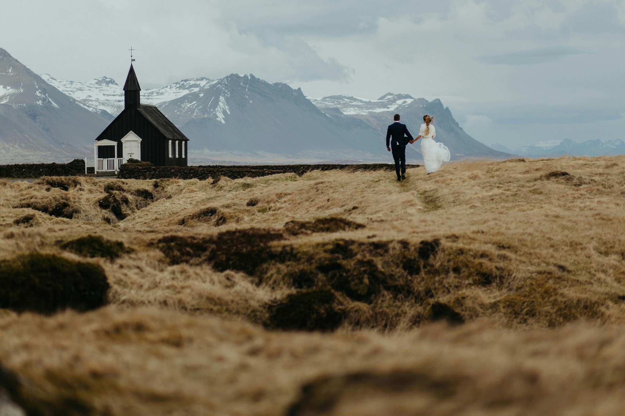 Bride and groom walking toward Búðir Black Church during fall in Iceland.
