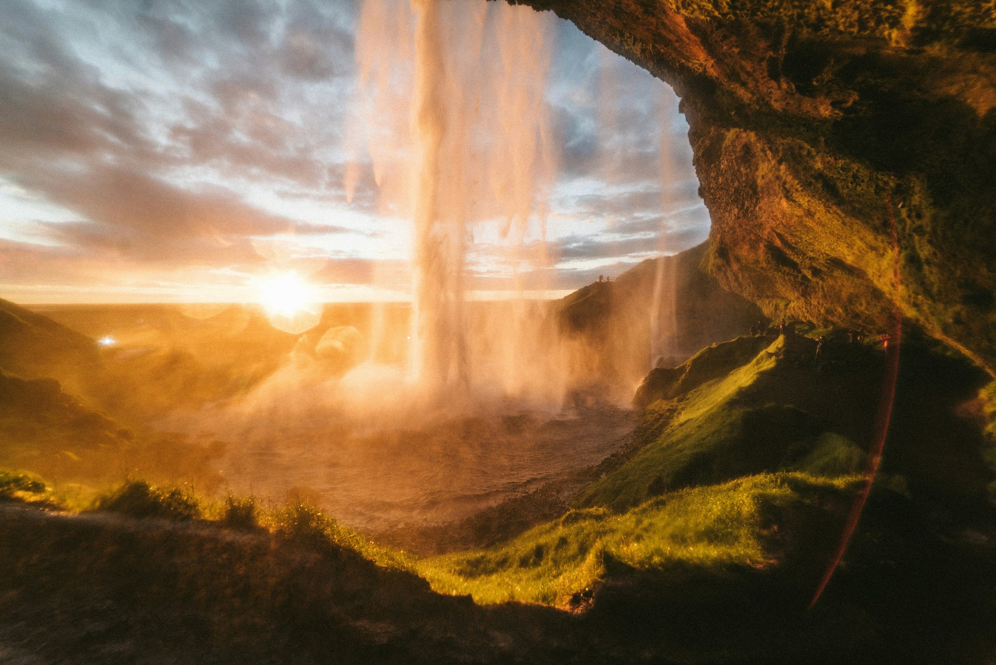 View from behind Seljalandsfoss Waterfall with golden sunlight glowing through the falling water.