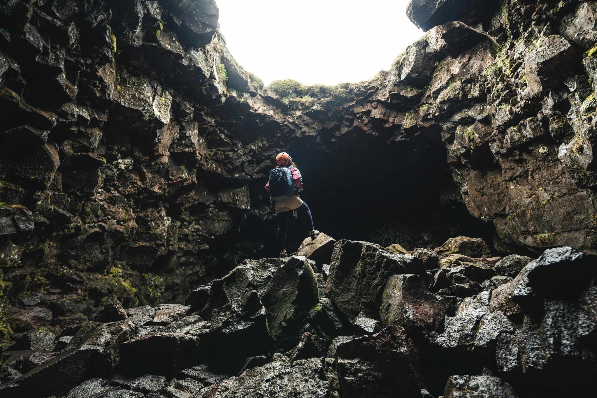A woman standing beneath a cave opening in the Raufarhólshellir Lava Tunnel in Ölfus, Iceland.