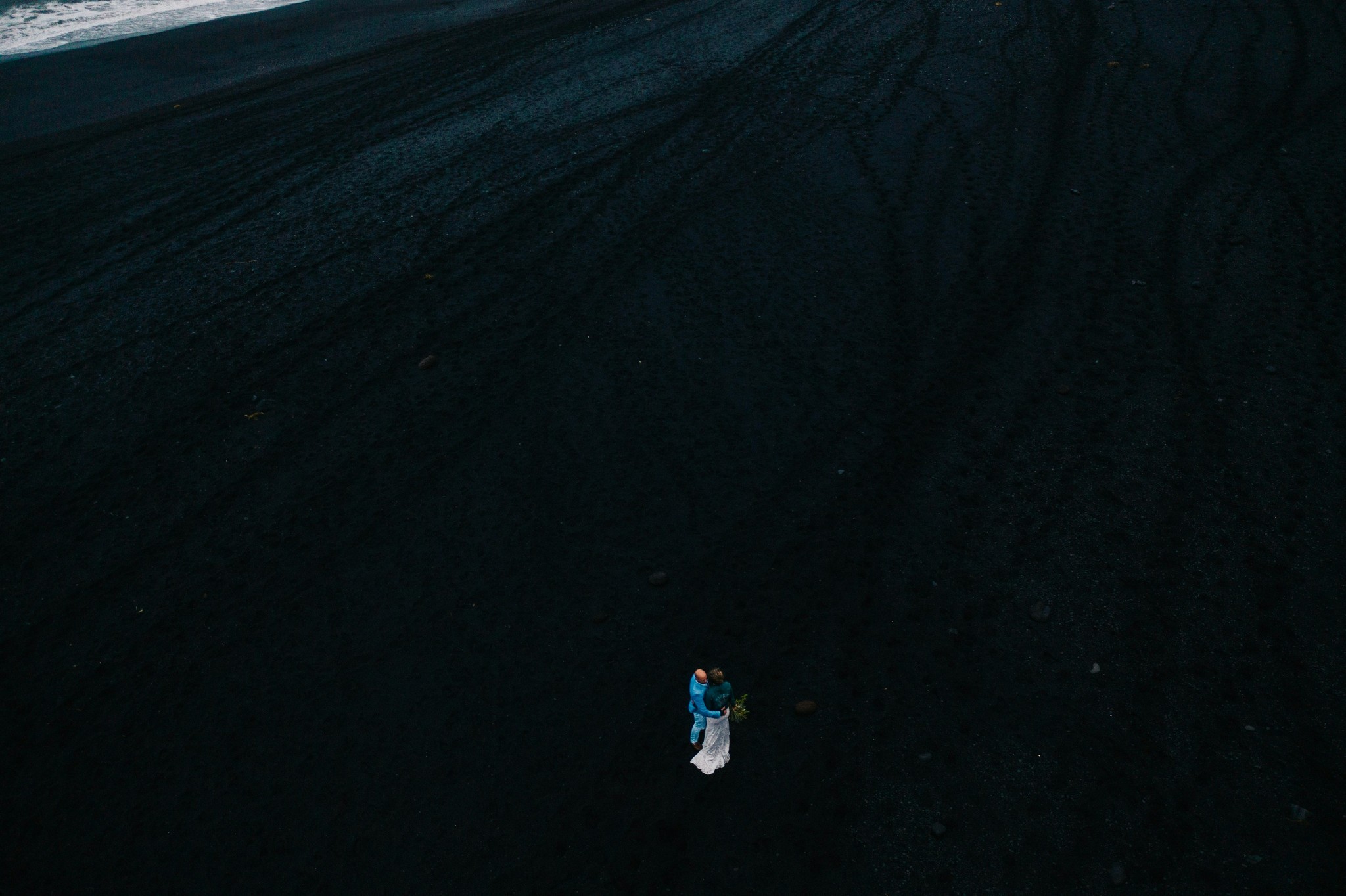 Wedding couple walking along a black sand beach in Iceland.