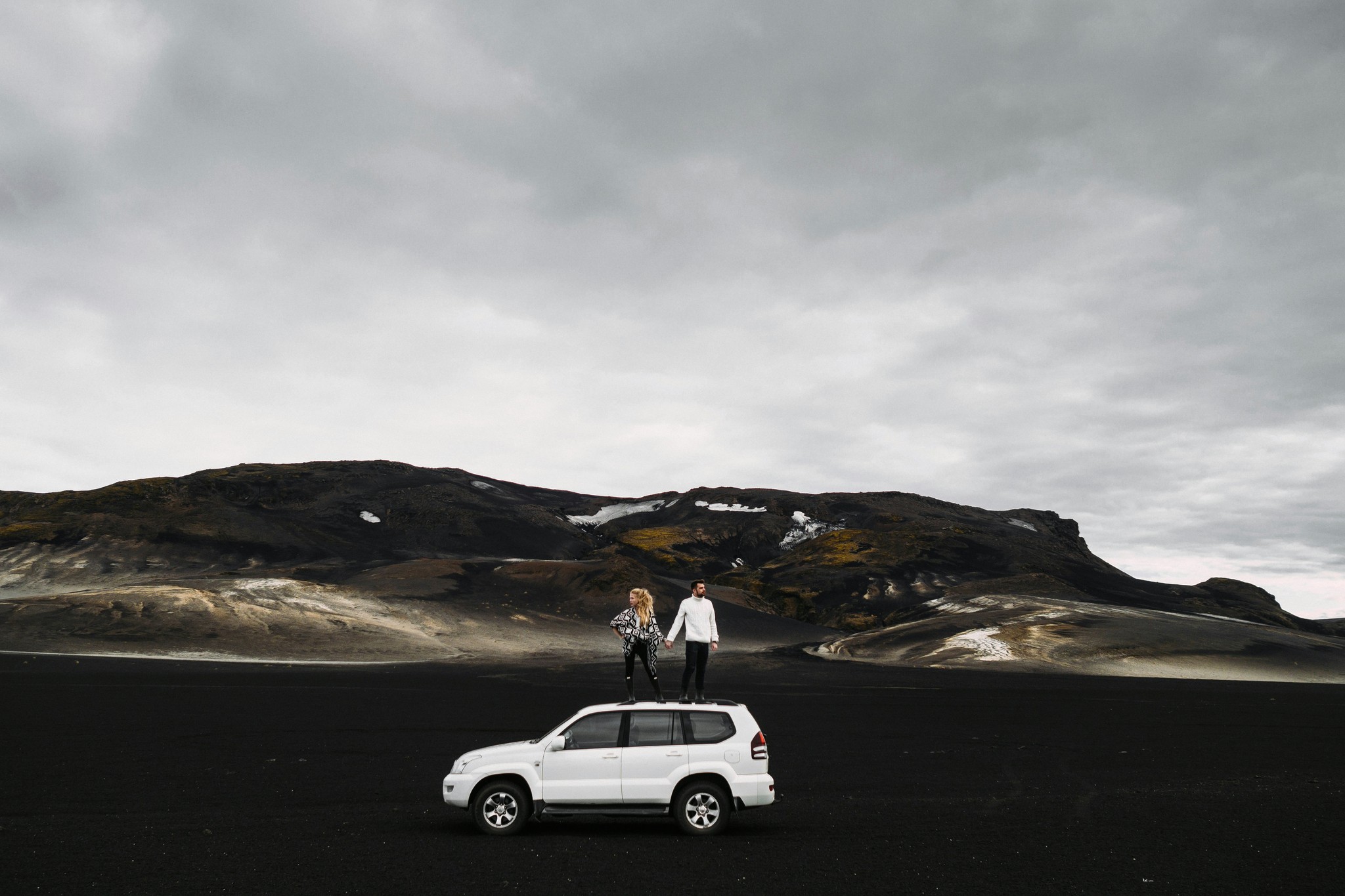 A couple holding hands on top of an SUV in the Icelandic Highlands.
